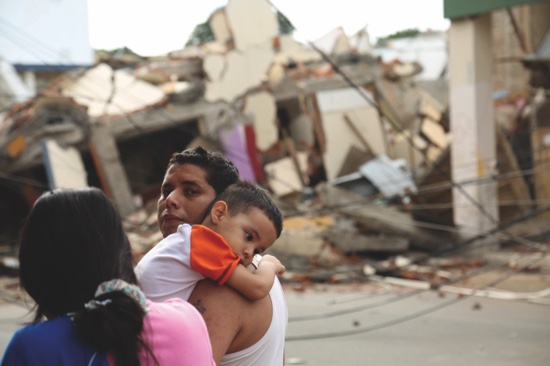 A man holds a child next to a collapsed building caused by a 7.8 earthquake in Portoviejo